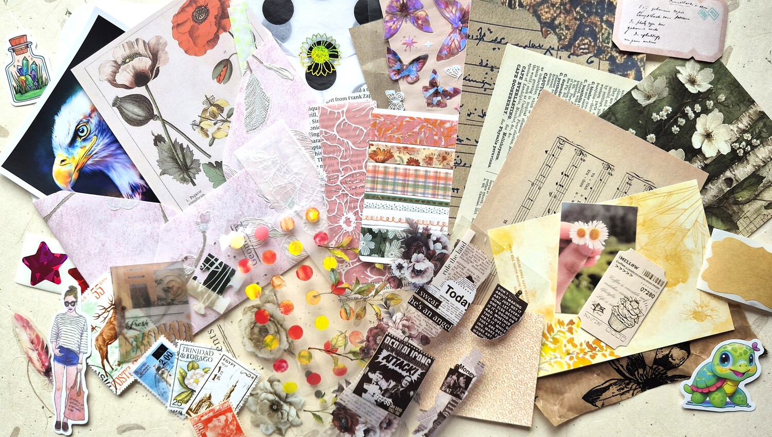 A flatlay of postcard decorating supplies: stickers, washi tape, vintage stamps, ephemera and paper cuts